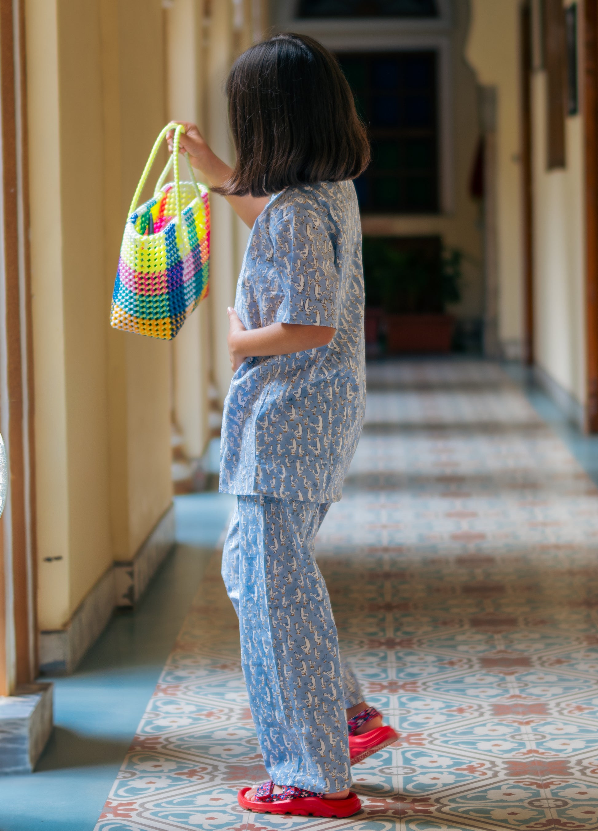 Child holding a colorful woven bag in a hallway