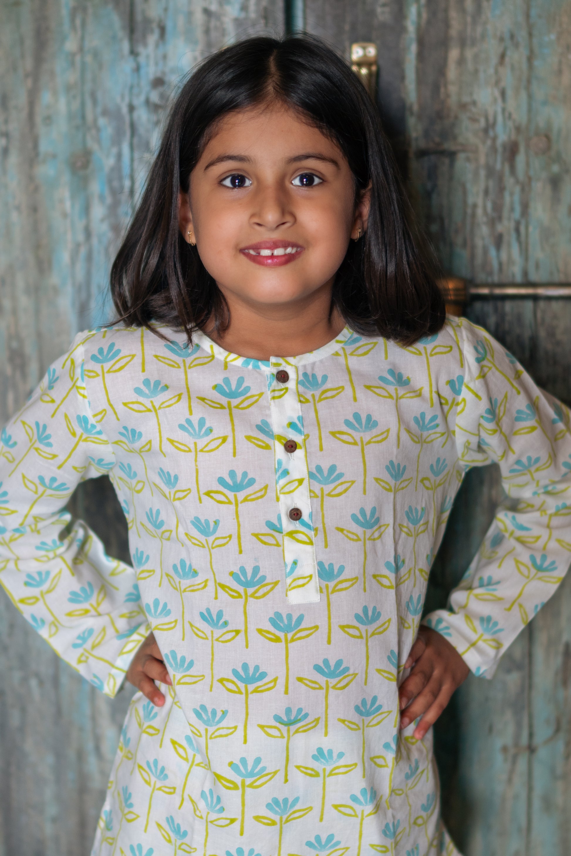 Young girl wearing a floral-patterned nightsuit with a wooden door in the background
