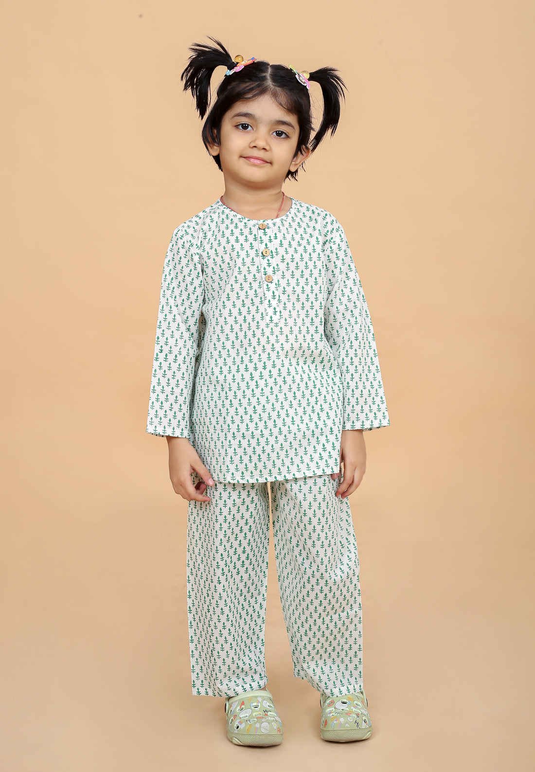 A girl wearing a green booti hand block printed night suit with round neck and half button placket, along with full sleeves and side slits. The set includes matching pajamas with an elasticated waistband.
