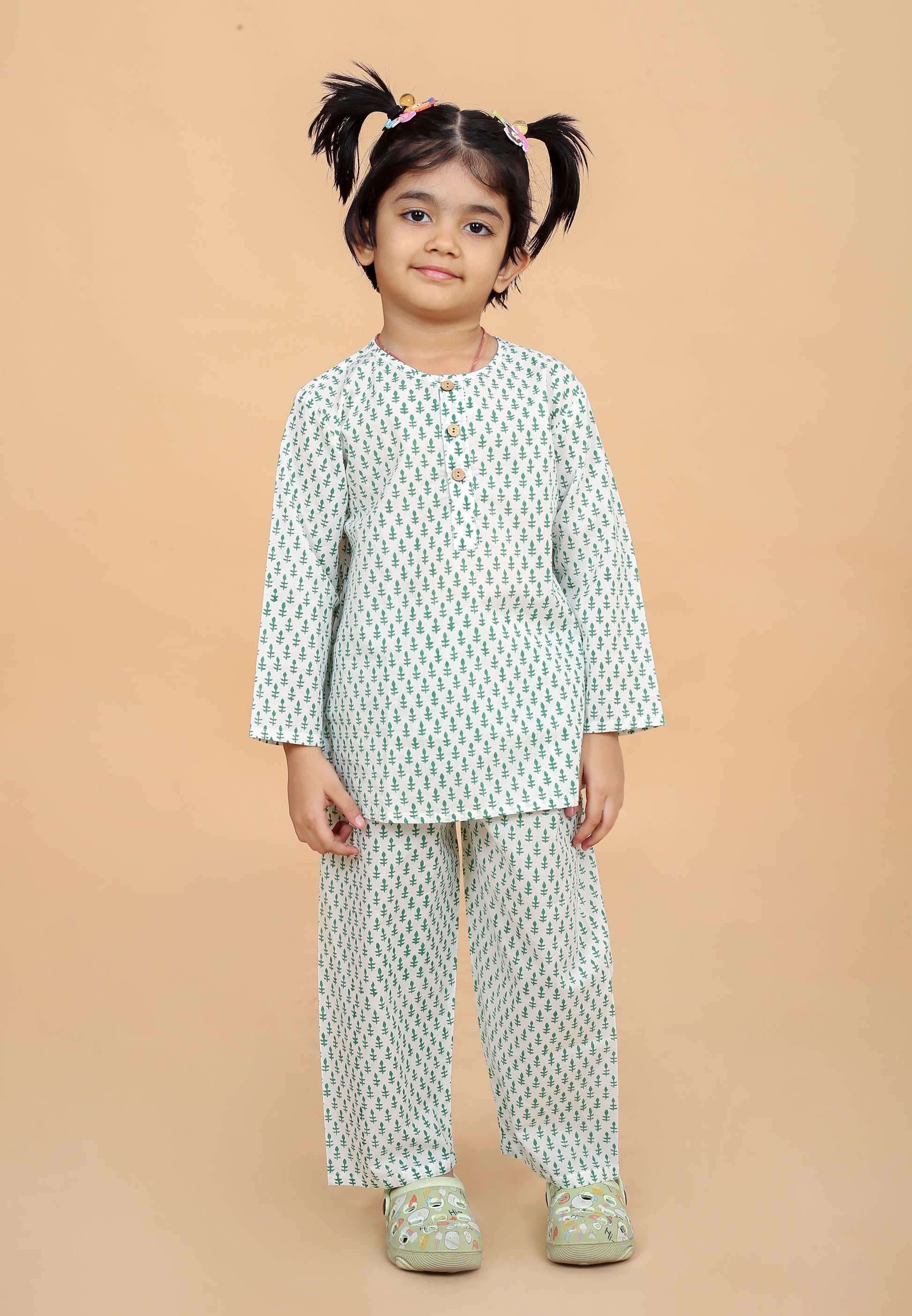 A girl wearing a green booti hand block printed night suit with round neck and half button placket, along with full sleeves and side slits. The set includes matching pajamas with an elasticated waistband.
