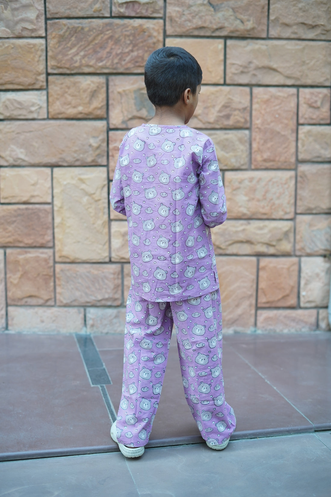 Child wearing a purple teddy pajama set with cartoon characters on a stone floor.