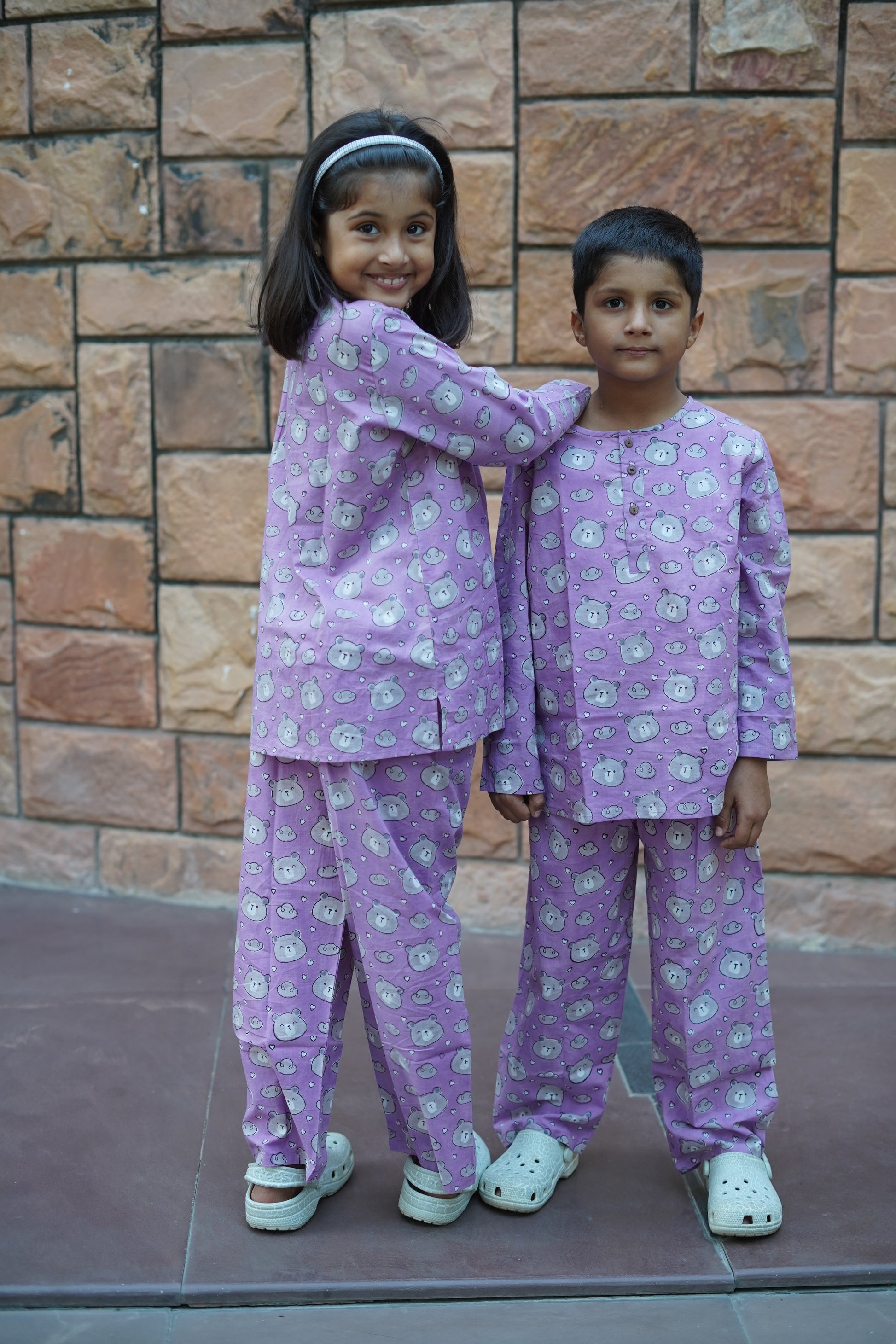 Two children in matching purple outfits standing on a tiled floor.