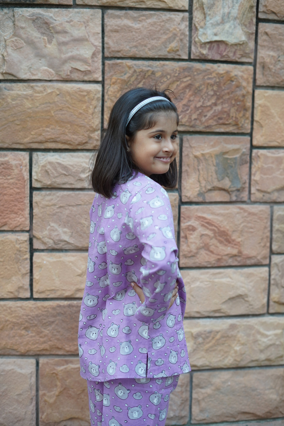 Child wearing a purple teddy pajama set with cartoon characters on a stone floor.